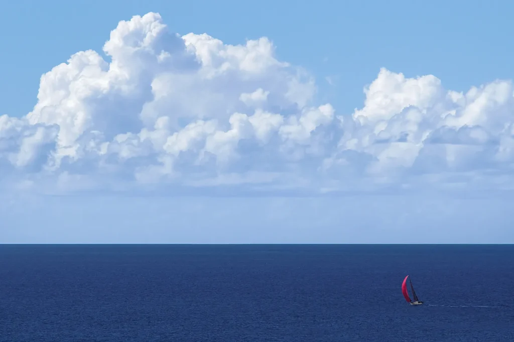 Sailing yacht with a red spinnaker at full sail on a blue ocean